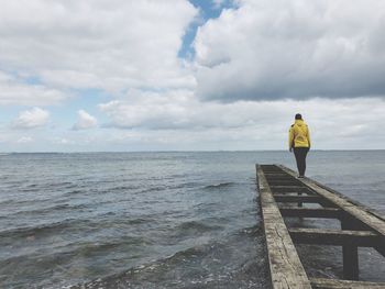 Rear view of man standing on pier over sea against sky