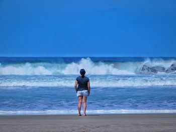 Rear view of woman standing at beach on sunny day