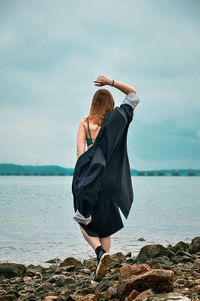 Rear view of woman standing on rock at beach against sky