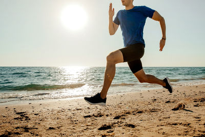 Low section of man running on shore at beach