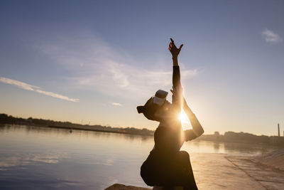 Low angle view of silhouette woman standing by lake against sky during sunset