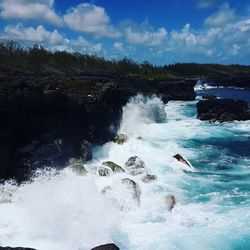 Water splashing on rocks against sky