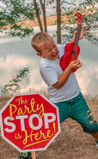 Boy playing ukelele while standing by information sign with text