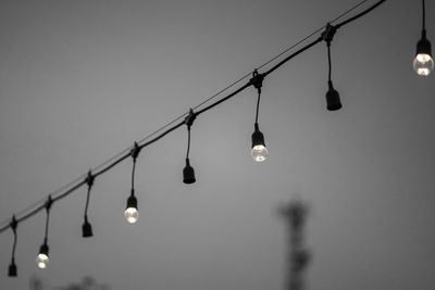 Low angle view of light bulbs hanging against clear sky