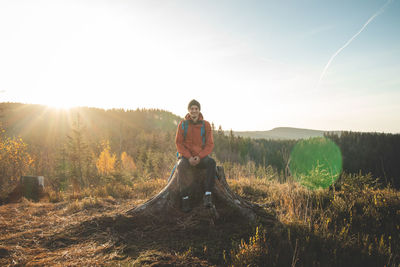 Active hiker sitting on a stump enjoys the feeling of reaching the top of the mountain at sunrise. 