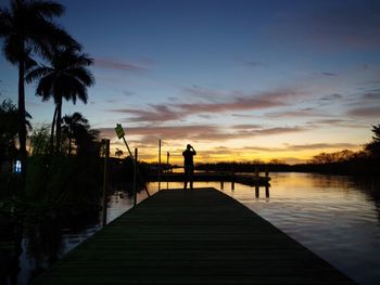 Silhouette man standing on pier over lake against sky during sunset