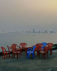 Empty chairs and tables on beach against sky at dusk