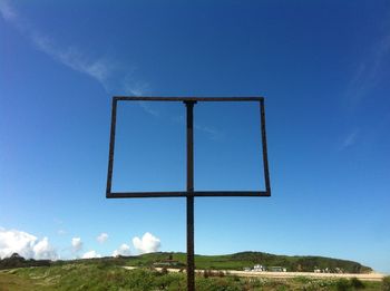 Low angle view of cross on land against blue sky