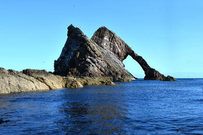 Rock formation in sea against clear blue sky