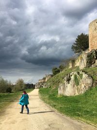 Rear view of woman walking on footpath against cloudy sky