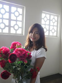 Portrait of smiling young woman standing by flowers at home