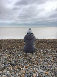 Rear view of woman sitting  on beach with dramatic clouds