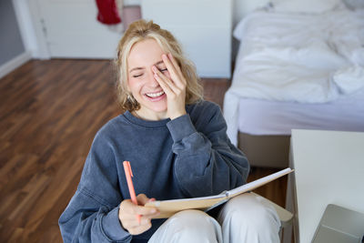 Portrait of young woman using laptop while sitting on bed at home