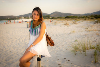 Portrait of young woman standing at beach against sky