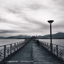 Pier over river against cloudy sky