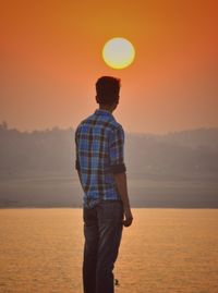 Rear view of man standing at sea during sunset