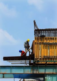 Low angle view of workers working at construction site against sky