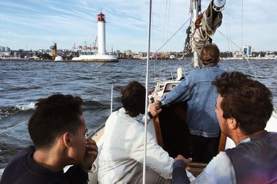 People sitting on sailboat by sea against sky