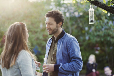 Couple talking while holding drink bottles at summer party