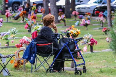 Side view of disabled woman sitting on chair by mobility walker in park