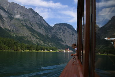 Side view of man sitting on window by lake