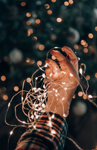 Close-up photo of female hands holding fairy lights in front of christmas tree