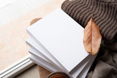  stack of white blank books with autumn leaves and cup of hot tea on old wooden chair, mockup design