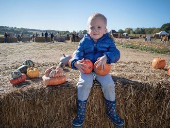 Full length of boy holding pumpkins on hay at field