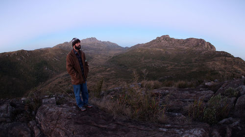 Male hiker in warm clothing looking away while standing on mountain