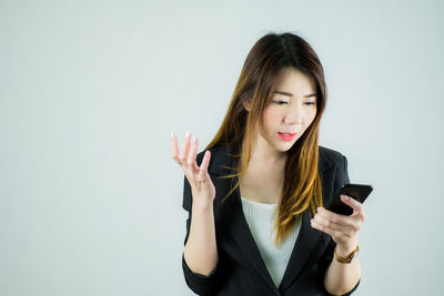 Young woman using phone while standing against white background