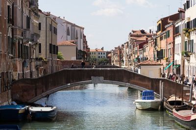 Boats in canal amidst buildings in city against sky