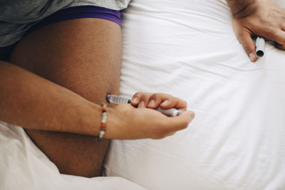 Cropped image of man injecting insulin on lap while sitting on bed at home