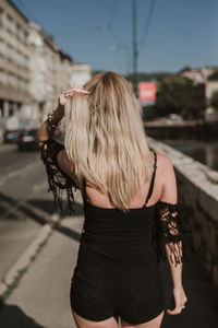 Rear view of woman with blond hair standing in city