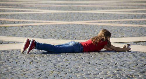 Full length of woman photographing while lying on street