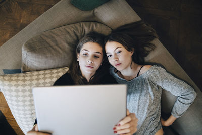 High angle view of girls using laptop while lying on sofa at home