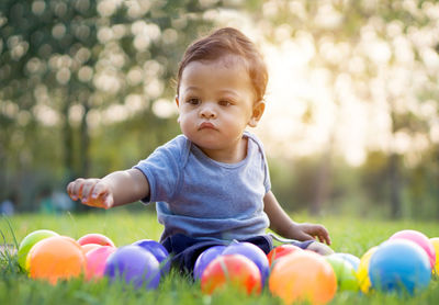Cute baby boy sitting amidst colorful balls on field