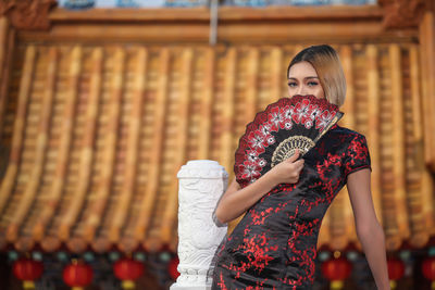 Portrait of woman holding folding fan while standing on building terrace