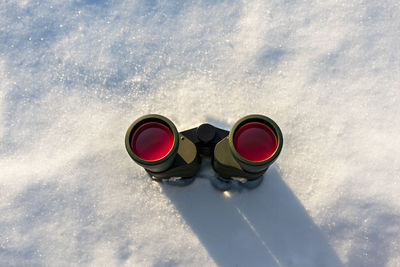 Black binoculars with red lens on white snowy winter background copy space birdwatching ecology