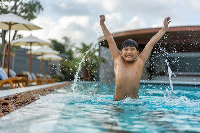 Asian young boy having a good time in swimming pool, he jumping and playing a water in summer.