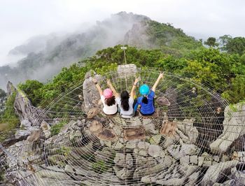 High angle view of female friends sitting on cliff against tree mountains