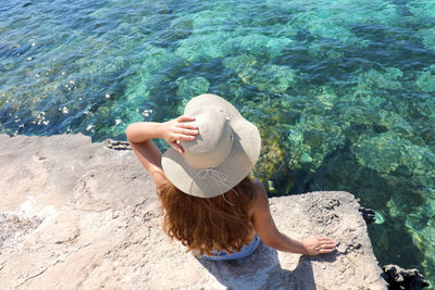 High angle view of woman sitting on rock at sea shore