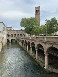 Arch bridge over river by building against sky