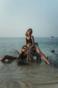 Side view of woman sitting in sea against sky