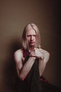 Shirtless man sitting against brown background