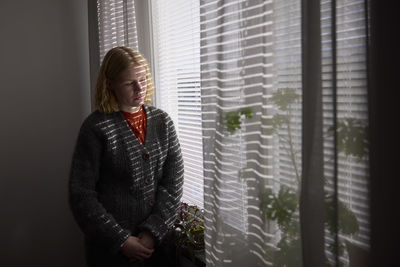 Pensive teenage girl looking through window