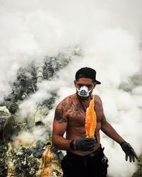 Shirtless man wearing mask standing against smoke