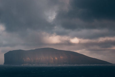 Scenic view of sea by mountain against sky