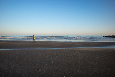 Side view of woman walking at beach against clear sky during sunset