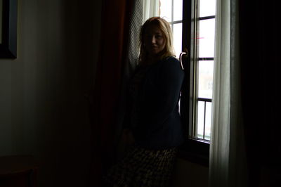 Portrait of woman standing by window at home