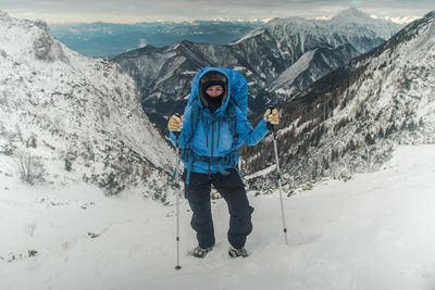 Woman hiking uphill on snowcapped mountain against sky